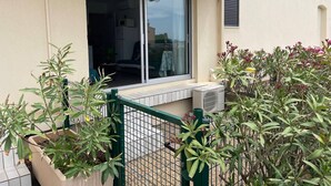 A building with a large window, a green metal fence, and potted plants. - Studio with AC and pool - 4 guests (Cap d'Agde)