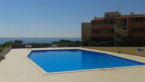 A rectangular swimming pool with a tiled deck, a wooden fence, and a view of the sea. - Studio with AC and pool - 4 guests (Cap d'Agde)