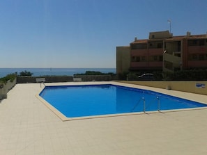 Ein rechteckiger Pool mit Fliesen umrandet, einem Holenzaun und Blick auf das Meer.