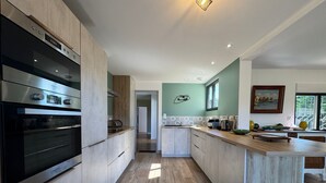 Une cuisine moderne dotée d’un îlot central, d’appareils électroménagers intégrés et offrant une vue sur l’extérieur.