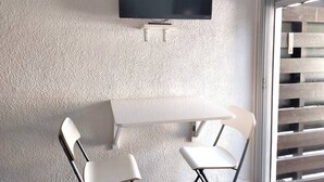 Et værelse med et fladskærms-tv monteret på væggen, et hvidt bord og to hvide stole.