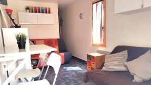 Un espacio habitable compacto con kitchenette, zona de comedor, sofá y ventana con cortinas.