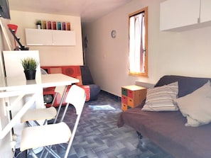 A compact living space with a kitchenette, a dining area, a sofa, and a window with curtains. - Ideal studio in Roquille - 4 guests (Cap d'Agde)