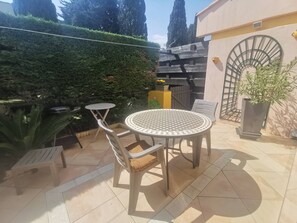 A patio with a round table and chairs, a small table, a potted plant, and a metal spiral staircase. - Apartment with pool access - 4 guests (Cap d'Agde)