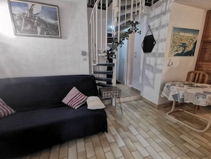 A living room with a dark sofa, a small table, a staircase, and a wall-mounted plant. - Quiet terraced house - 4 guests (Cap d'Agde)