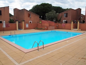 A rectangular swimming pool with two ladders, surrounded by a tiled deck and adjacent buildings. - Quiet terraced house - 4 guests (Cap d'Agde)