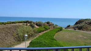 Paisaje costero con una vista despejada del mar, un camino que lleva a una zona rocosa y un farol.