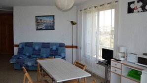 Una habitación con una mesa, sillas, un sofá, un televisor, una cafetera y un ordenador.