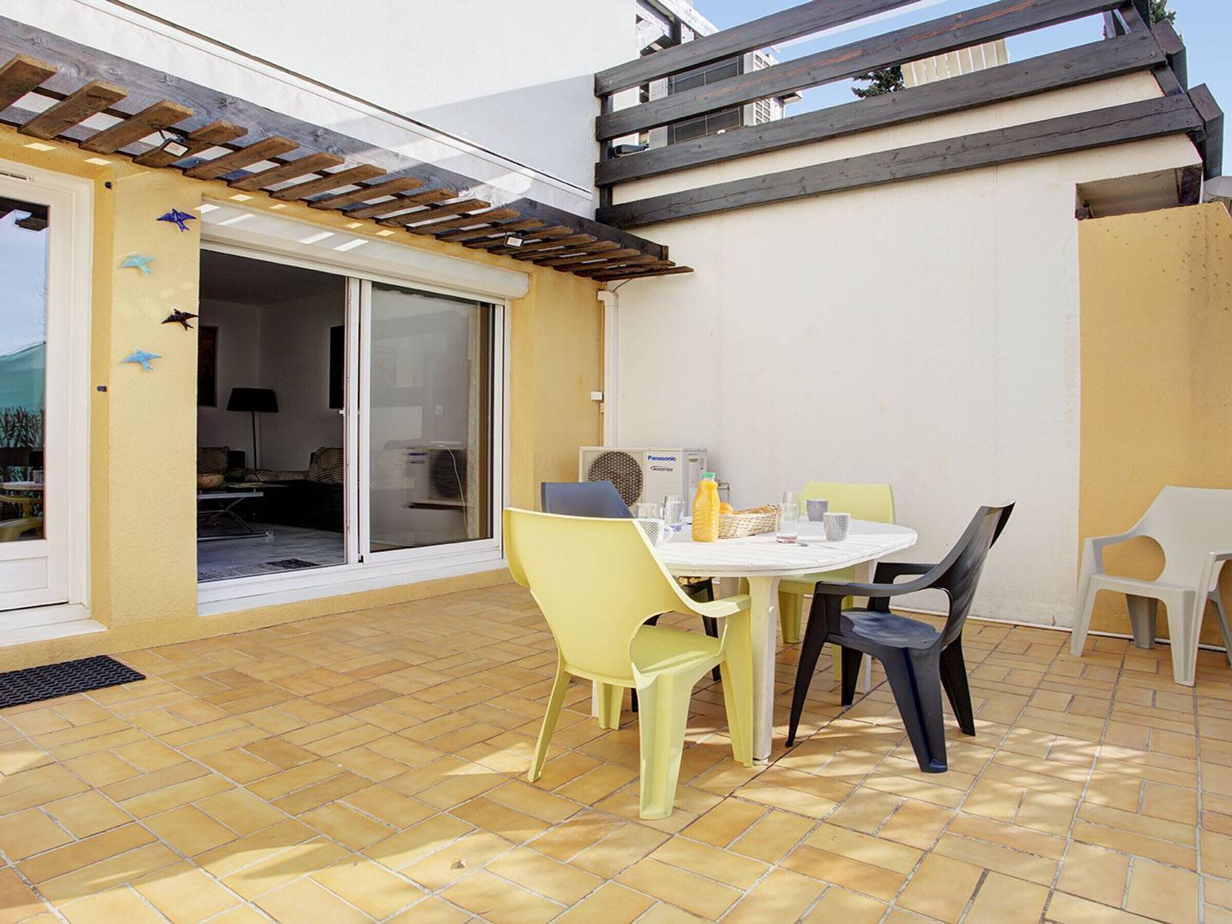 Un patio con mesa y sillas, una puerta corrediza de vidrio y una pérgola de madera.