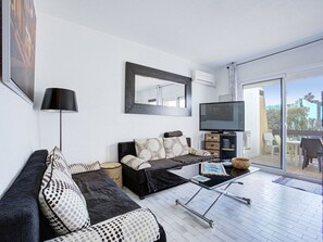 A modern living room with a sofa, coffee table, TV, and a balcony with outdoor furniture. - Apartment with air conditioning - 4 guests (Cap d'Agde)