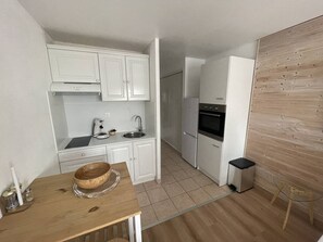 A compact kitchen with white cabinets, a wooden table, a sink, a coffee maker, and a refrigerator. - Studio with port view - 2 guests (Cap d'Agde)