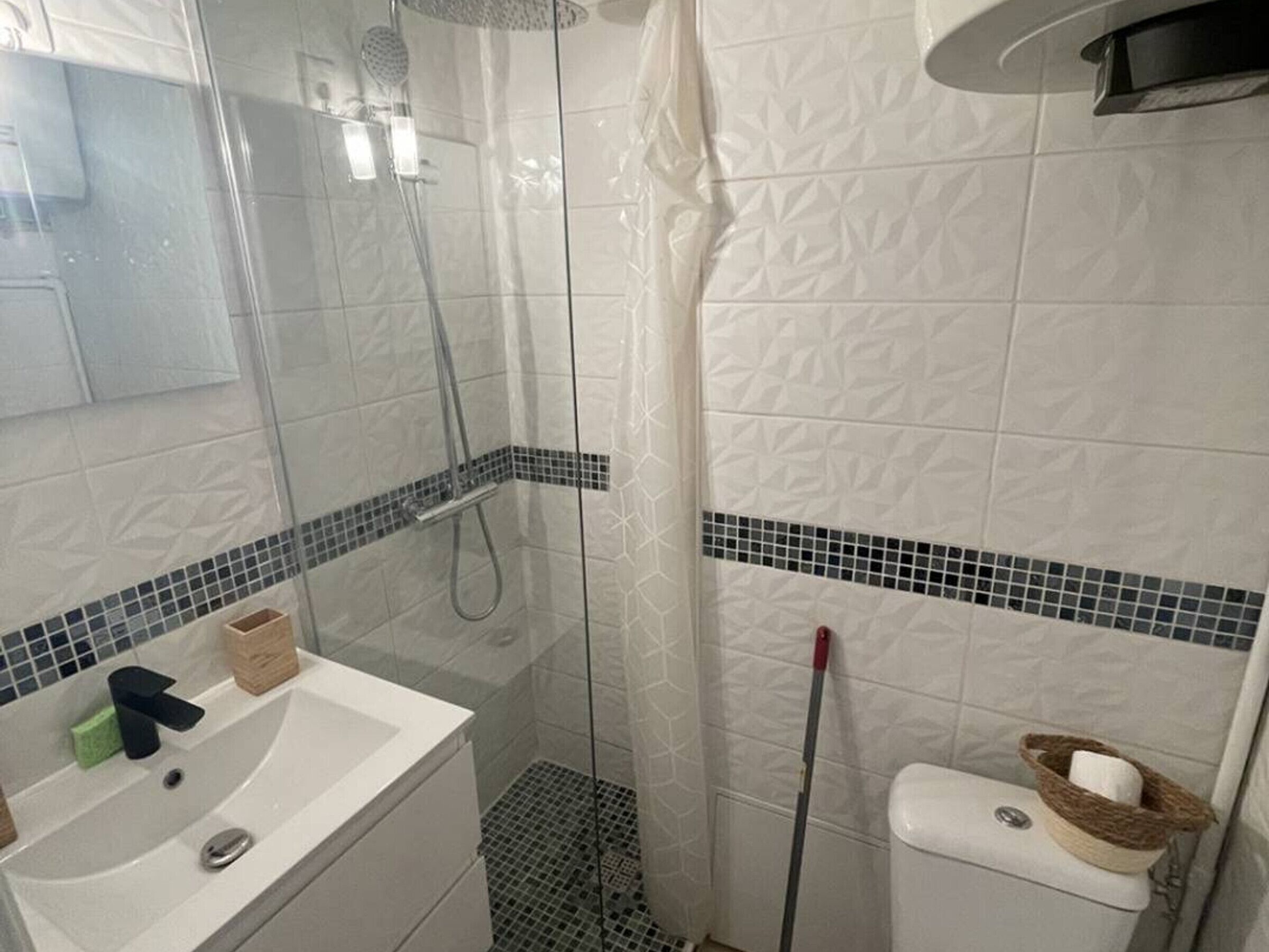 A bathroom with a shower, sink, toilet, and a mop leaning against the wall.