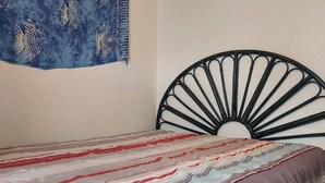 Ein Bett mit einem gemusterten Überwurf, einem schwarzen Metall-Kopfstück und einer Wanddekoration mit Fischmotiven.