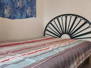 Ein Bett mit einem gemusterten Überwurf, einem schwarzen Metall-Kopfstück und einer Wanddekoration mit Fischmotiven.