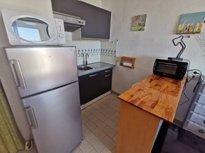 Eine kleine Küche mit Kühlschrank, Mikrowelle, Spüle und Holzarbeitsplatte.
