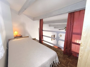A bedroom with a bed, a nightstand with a lamp, a wooden floor, a window with curtains, and a view of a balcony. - 3-room villa with parking - 7 guests (Cap d'Agde)