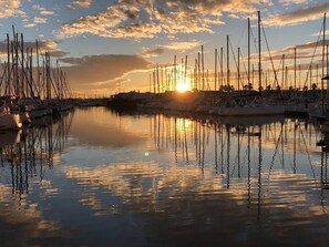 Ein Yachthafen mit mehreren vertäuten Booten, ruhigem Wasser und einem Sonnenuntergang im Hintergrund.