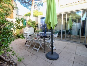 Eine Terrasse mit Tisch und Stühlen, einem grünen Sonnenschirm und einer Glastür, die zu einem Außenbereich führt.