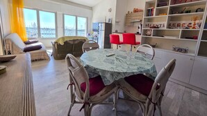Ett rymligt vardagsrum med ett matbord omgivet av stolar, en soffa och utsikt över en stadssiluett genom stora fönster.