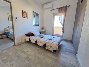 Ein Schlafzimmer mit Bett, Fenster mit Vorhängen, Nachttisch und einem kleinen Stuhl.