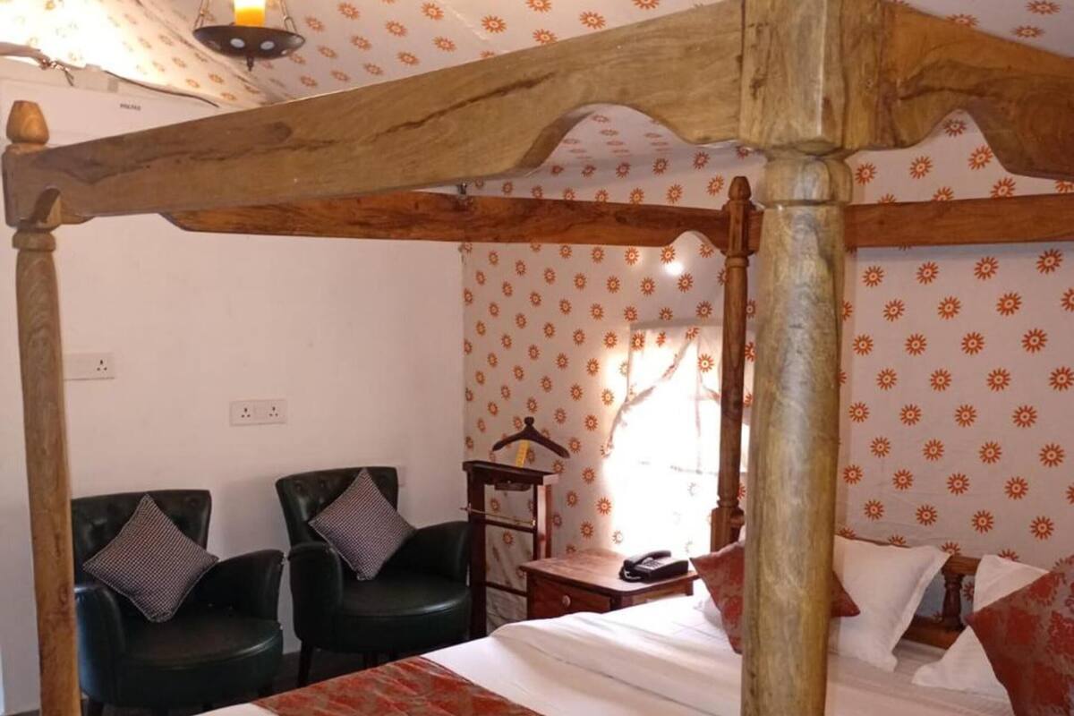 A four-poster bed with a wooden frame, a patterned wall, and a small table with a telephone.