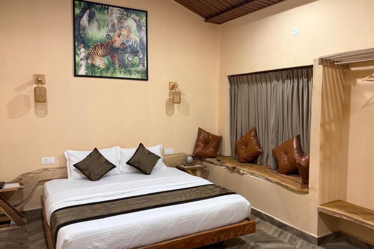 A bedroom with a bed, pillows, a window with curtains, a wooden bench, and a tiger painting on the wall.