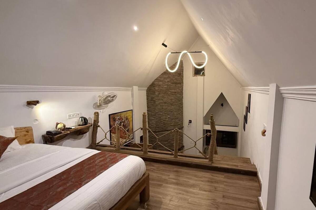 A bedroom with a bed, a wooden floor, a stone wall, a staircase, and a mounted TV.