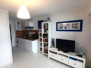 A compact living space with a kitchenette, a flat-screen TV, and a bookshelf. - Apartment with port view - 4 guests (Cap d'Agde)