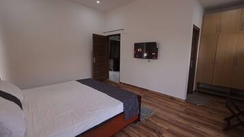 Een slaapkamer met een bed, een televisie, houten vloeren en een kledingkast.