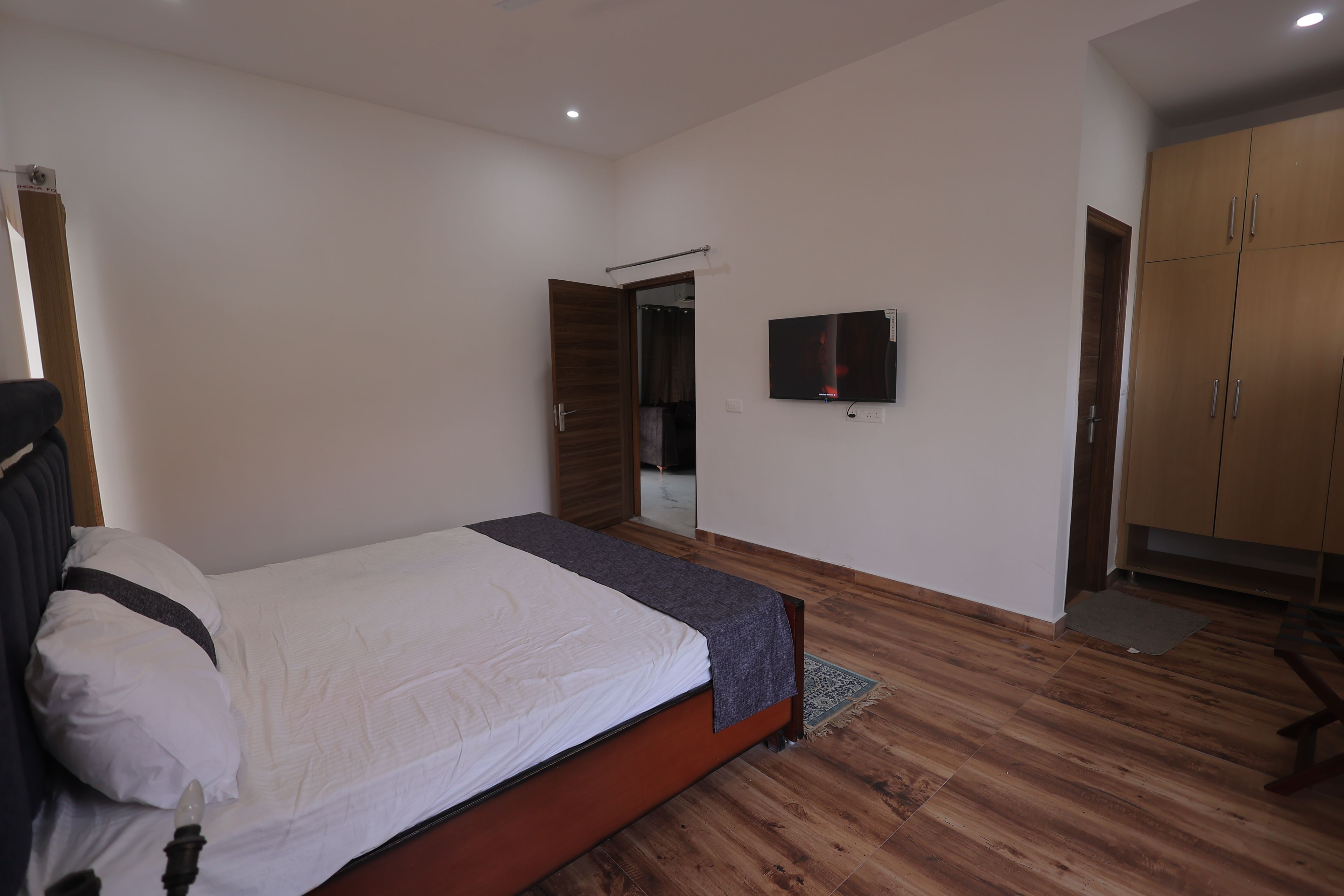 A bedroom with a bed, a television, wooden flooring, and a wardrobe.