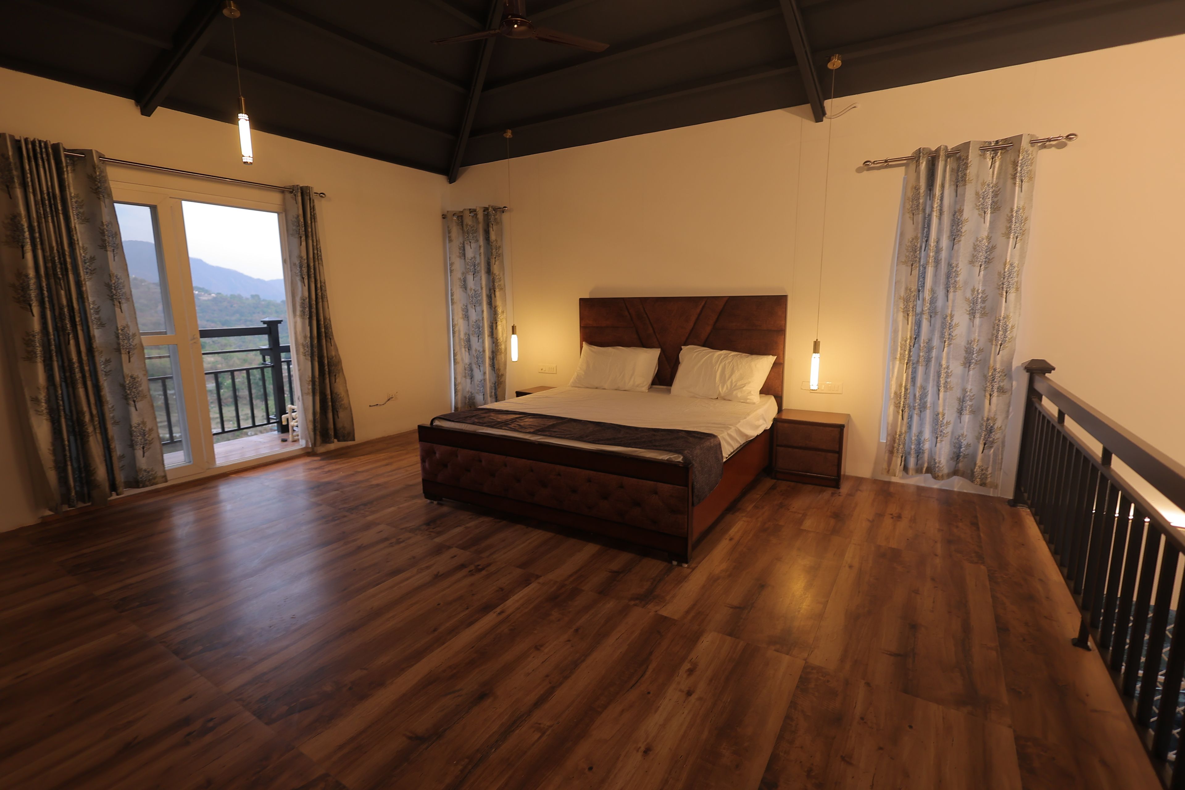 Une chambre avec un plancher en bois, un lit avec une tête de lit, une table de chevet et une fenêtre avec des rideaux.