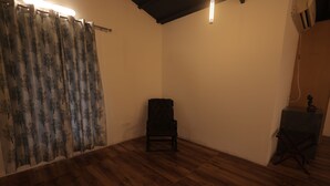 A room with wooden flooring, a black chair, a curtain with a tree pattern, and a ceiling light fixture. - Maktain Glance (Dehradun)