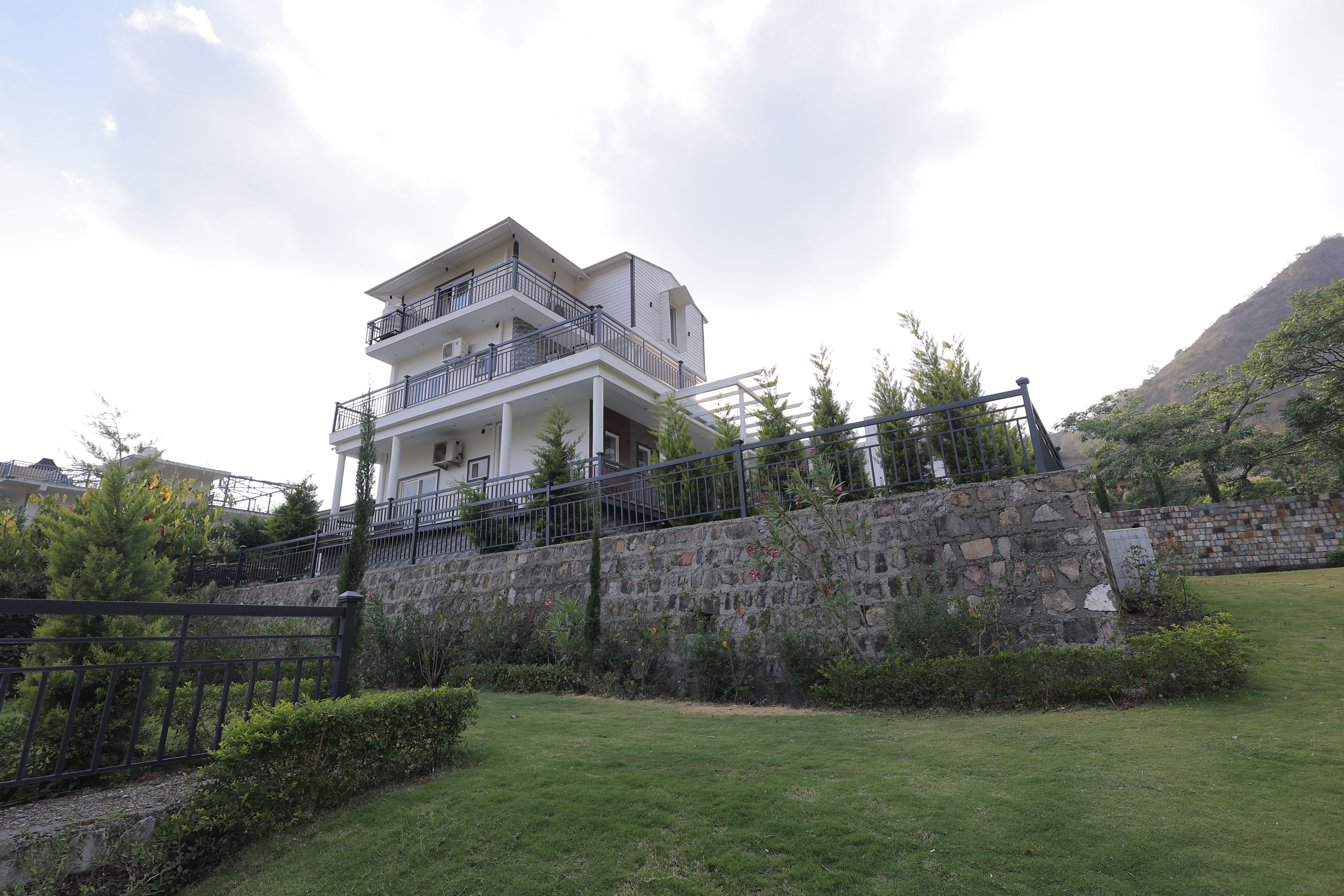 A multi-story building with balconies, a stone retaining wall, and a grassy area in front.