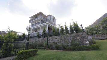 A multi-story building with balconies, a stone retaining wall, and a grassy area in front.