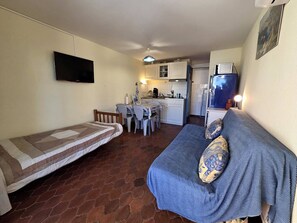 A compact living space with a kitchenette, a dining area, a sofa with patterned cushions, and a TV mounted on the wall. - Studio with AC, beach access - 3 guests (Cap d'Agde)