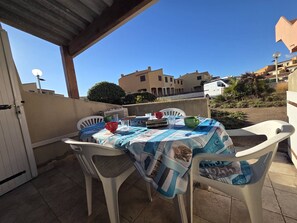 An outdoor patio with a table covered by a patterned tablecloth, surrounded by white plastic chairs. - Studio with AC, beach access - 3 guests (Cap d'Agde)