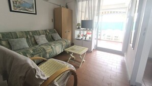 Un soggiorno con divano, due poltrone in legno, televisione e un balcone con vista.