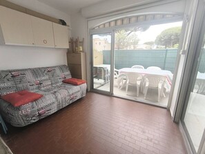 A room with a sofa, a table, chairs, and a sliding glass door leading to an outdoor area. - T2 apartment with AC - 4 guests (Cap d'Agde)