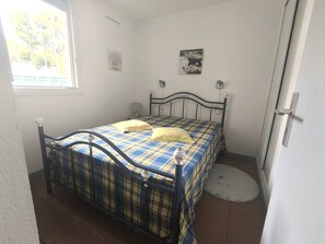 A bedroom with a bed, a window, a door, and a small round rug. - T2 apartment with AC - 4 guests (Cap d'Agde)