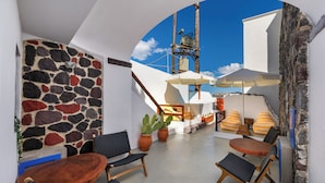 A sunlit outdoor seating area with stone walls, wooden furniture, and potted plants. - Orasis Houses- Luxury Retreats with Pool (Akrotiri)