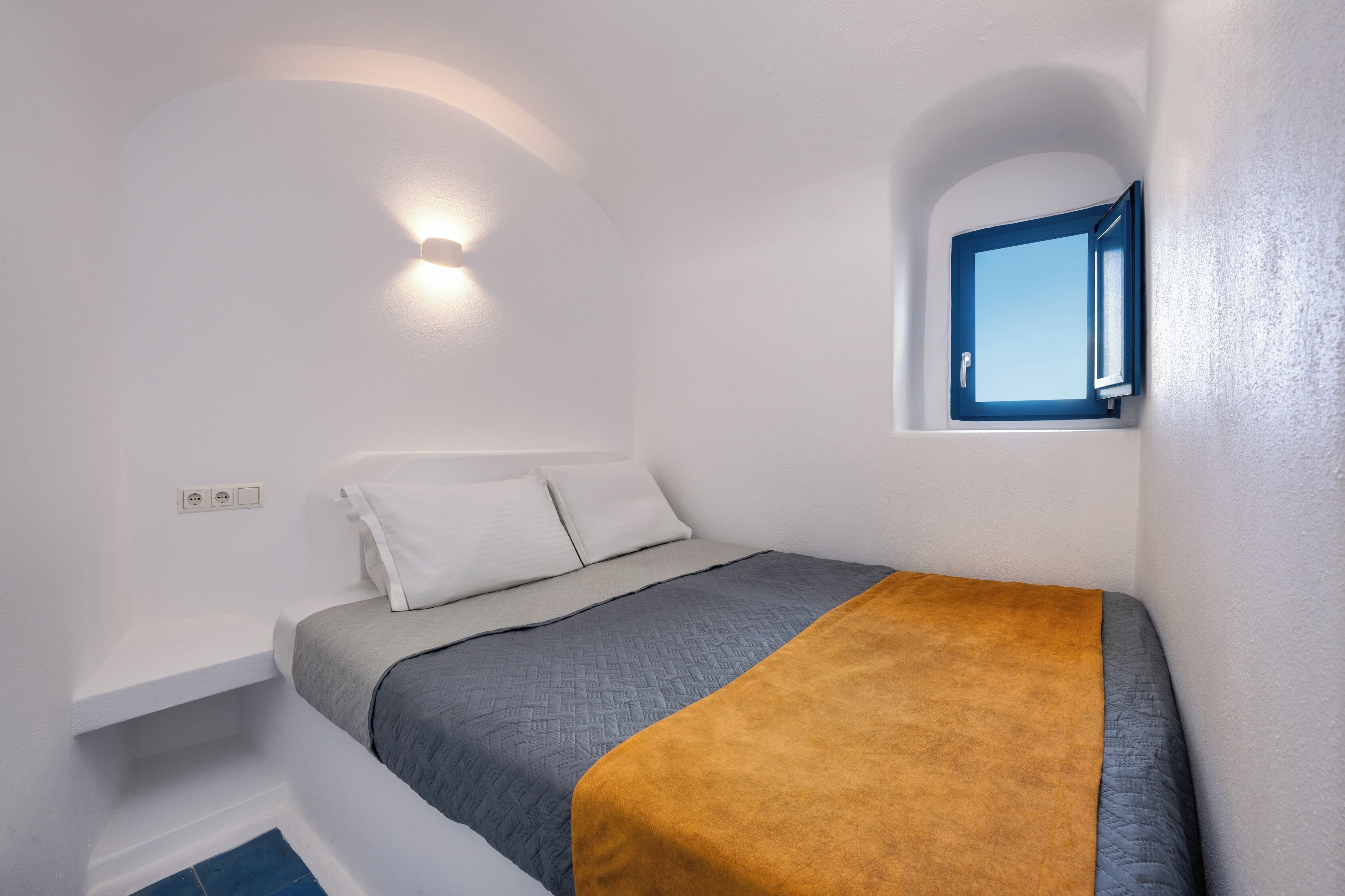 Un dormitorio con cama, ventana y una lámpara fijada a la pared.