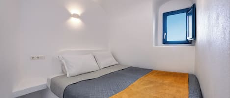 Un dormitorio con cama, ventana y una lámpara fijada a la pared.