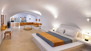 A modern bedroom with a large bed, a sofa, a small table, and a kitchen area in the background. - Orasis Houses- Luxury Retreats with Pool (Akrotiri)