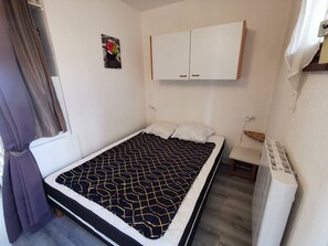 A single bed with a patterned bedspread, a small bedside table, a radiator, and a wall-mounted cabinet. - Studio cabin, parking, sea view - 5 guests (Cap d'Agde)