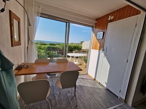 A balcony with a wooden table and chairs, a view of greenery and a building, and a white door. - Studio cabin, parking, sea view - 5 guests (Cap d'Agde)