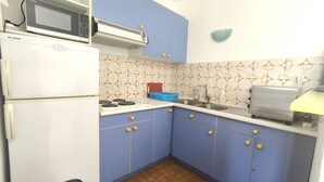 Una cucina compatta con frigorifero, microonde, fornello, lavello e tostapane.