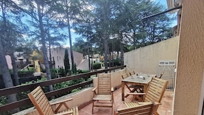 A balcony with wooden furniture, a view of trees and buildings, and a railing. - Family apartment near the pines - 6 guests (Cap d'Agde)