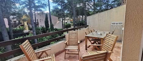 A balcony with wooden furniture, a view of trees and buildings, and a railing.