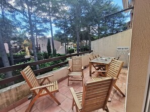 A balcony with wooden furniture, a view of trees and buildings, and a railing. - Family apartment near the pines - 6 guests (Cap d'Agde)