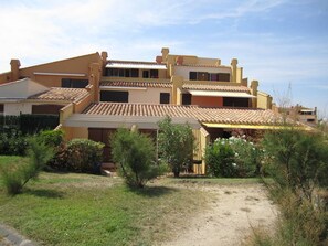 Ein mehrstöckiges Gebäude mit flachem Dach, einer überdachten Terrasse und einem Feldweg, der zum Eingang führt.